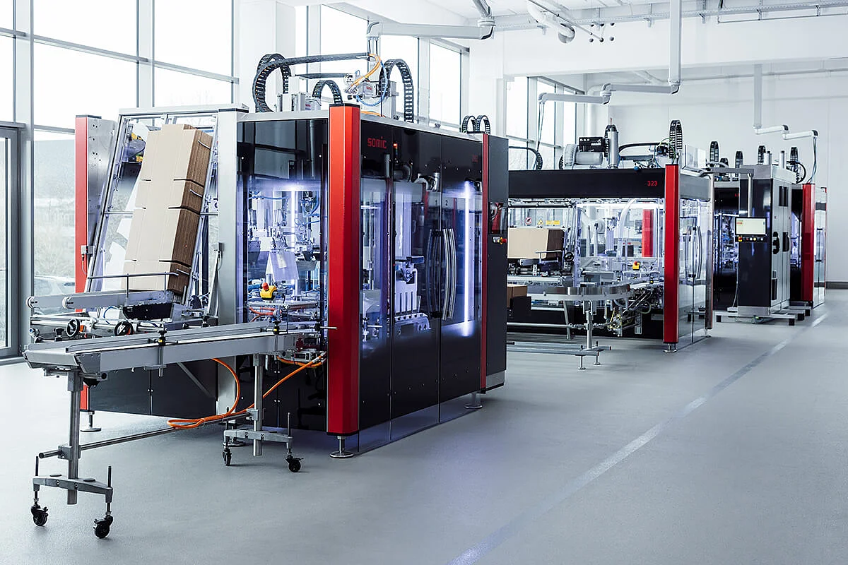 Mehrere SOMIC Karton-Verpackungsmaschinen in Reihe während der Inbetriebnahme in einer modernen Produktionshalle
