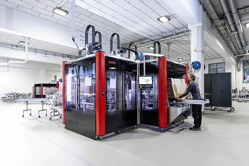 Person beim Befüllen des Kartonmagazins einer SOMIC 434 Kartoniermaschine.